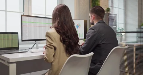 Finance team analyzing spreadsheets and charts on dual monitors in modern office Stock Footage 330778519