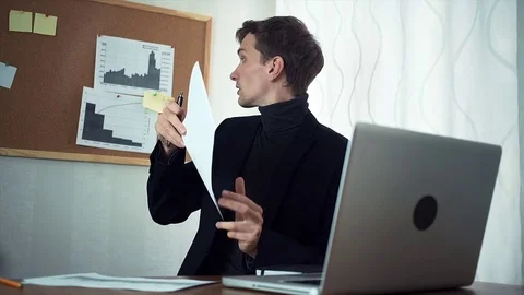 Financial analyst chatting with client using laptop demonstrating printed graphs Stock Footage 79900199