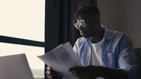 Financial analyst working on a report, reading documents in front of his laptop Stock Footage 304431438