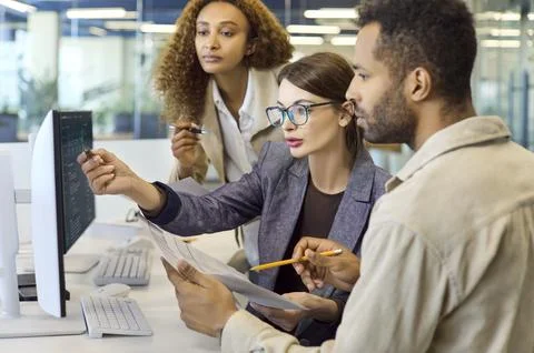Financial analysts team collaborating at computer with documents in office Stock Photos