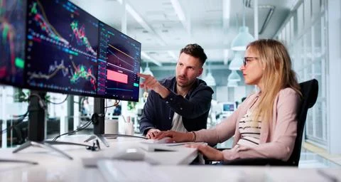 Financial Broker Analyzing Data On Multiple Computer Screens In Office Foto stock