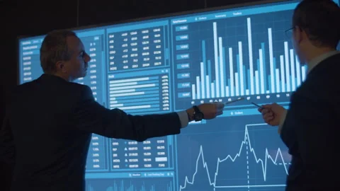 Financial data analysts analyzing charts on big screen Stock Footage 231577198