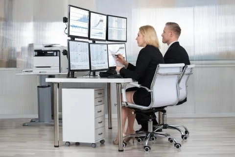 Financial workers analyzing data displayed on computer screens at desk in off 写真素材