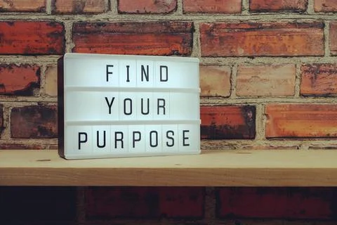 Find Your Purpose word in light box on brick wall and wooden shelves backgrou Stock Photos