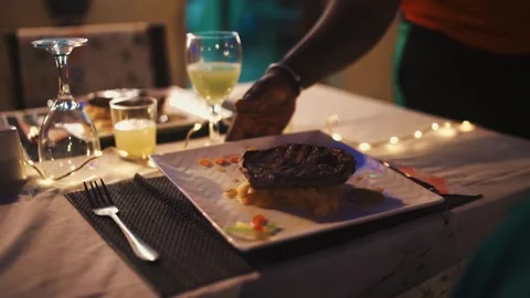 Fine Dining Service: Elegant Senegalese Waiter Serving Gourmet Steak Dish to Hap Stock Footage 309913858