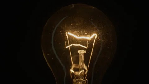Fine glowing thread brightens inside vintage light on isolated dark surface Stock Footage 332511046