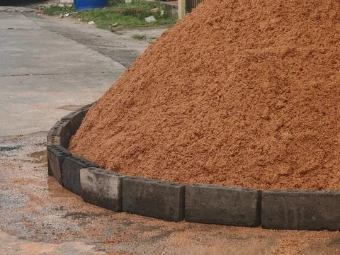 Fine reddish-brown sand held by a border of concrete blocks on a road surface. Stock Photos