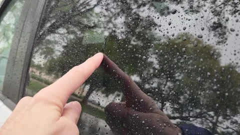 Finger drawing through raindrops on window glass with blurred street Stock Footage 331347318