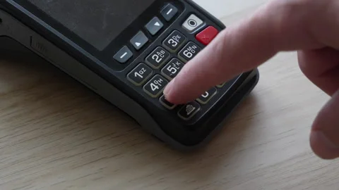 A finger enters a PIN code on the keypad of a black card payment terminal Stockbeeldmateriaal 347744552