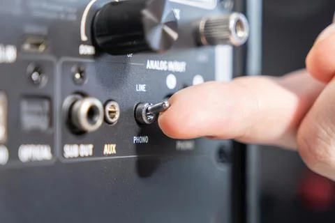 A finger flipping a phono line toggle switch on a black audio amplifier back Stock Photos