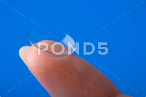 Finger holding contact lens over blue background Stock Photos