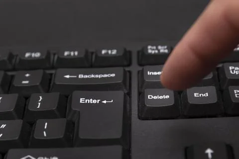 Finger next to Delete button. Removing unnecessary. Black keyboard on black b Stock Photos