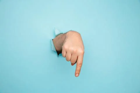 Finger pointing down through torn blue paper wall. Hand gestures of direction Stock Photos