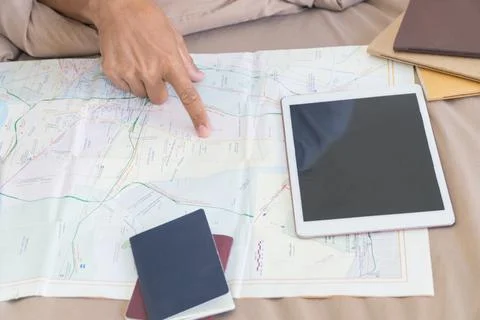 Finger pointing on a map spread out on the bed with book and tablet. Stock Photos