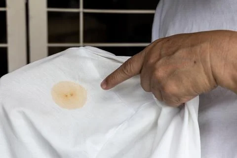 Finger pointing patch of brown stain on white t-shirt Stock Photos