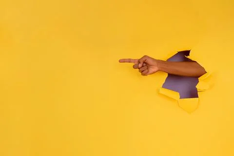 Finger pointing something through a hole in a paper wall. Stock Photos