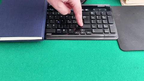 Finger Points to Enter Key on Black Keyboard Over Green Tabletop Surface Vidéo 327775164