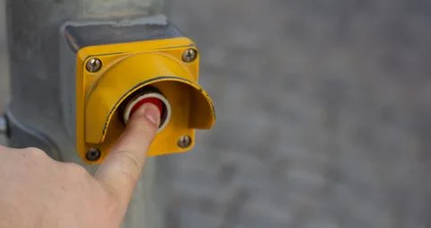 Finger presses red button in yellow case on metal pole Stock Photos