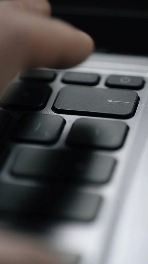 A finger pressing a Backspace key on a silver laptop keyboard. Vertical video. Stock Footage 325705004