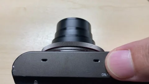 Finger push on camera to power on for lens to zoom on wooden table Video stock 248664244