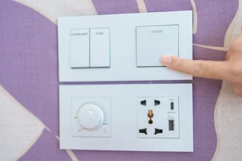 Finger pushing for turn on light switch on white wall at home room. Woman h.. Stock Photos