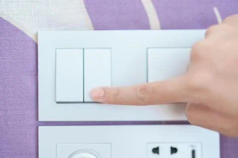 Finger pushing for turn on light switch on white wall at home room. Woman h.. Stock Photos