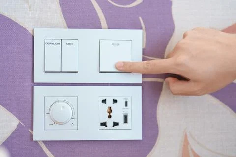 Finger pushing for turn on light switch on white wall at home room. Woman h.. Stock Photos