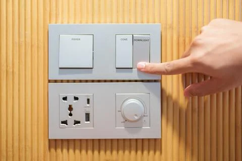 Finger pushing for turn on light switch on white wall at home room. Woman h.. Stock Photos