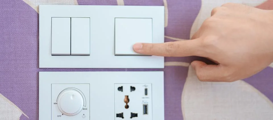Finger pushing for turn on light switch on white wall at home room. Woman h.. Stock Photos