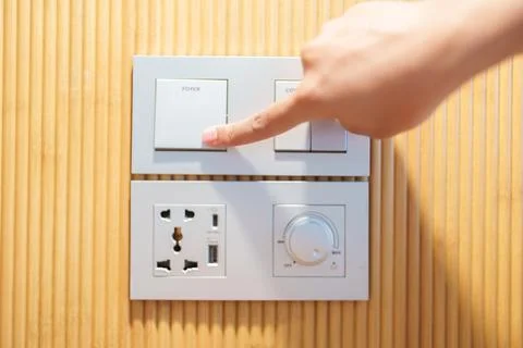 Finger pushing for turn on light switch on white wall at home room. Woman h.. Stock Photos