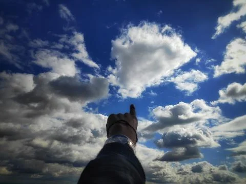 Finger Reaching Toward Clouds in a Blue Sky Stock-Fotos
