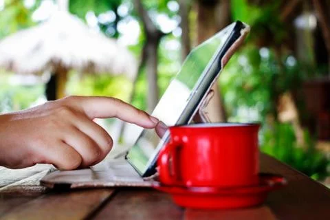 Finger touching on tablet with red cup on table in garden Stock Photos