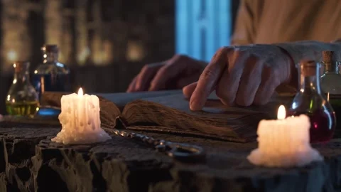Finger tracing ancient spellbook by candlelight in a stone chamber. 動画素材 310336782
