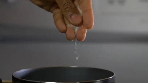 Fingers Adding Salt To The Sauce Pan Against A White Background Video stock 111040378