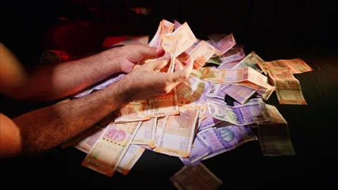 Fingers arrange 200 bills while 100 notes rest under light Stock Footage 313671025