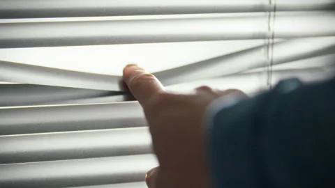Fingers brushing lightly against textured blinds in a softly lit interior se Stock Footage 323805355