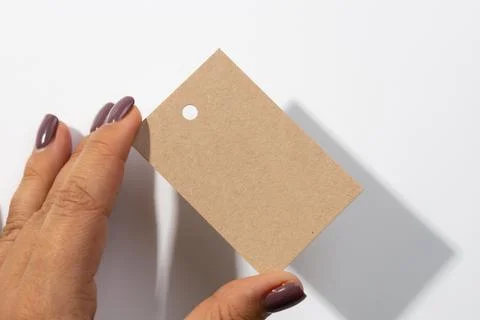 Fingers holding cardboard blank rectangular label tag with small hole in upper 스톡 사진
