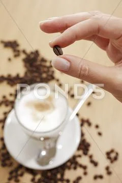 Fingers holding a coffee bean over a glass of Latte Machhiato Stock Photos