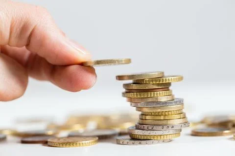Fingers holding coin over the stack of money from close up Stock Photos