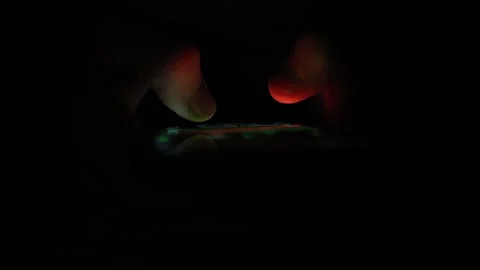 Fingers hover over a glowing smartphone screen in total darkness highlighting la Stock Footage 313842834