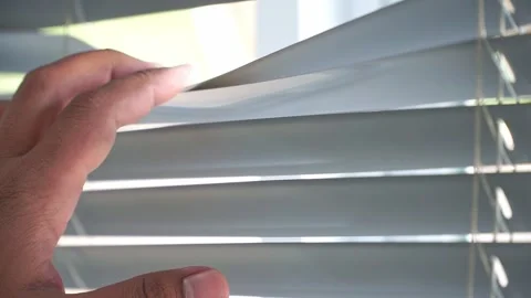 Fingers opening window blinds, allowing natural sunlight to enter. Stock Footage 339122017