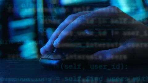 Fingers poised on a mouse, code streams in the blur behind. Stock Photos