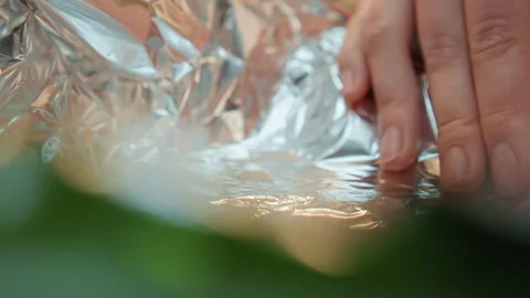 Fingers press foil edges securely. Gently pressing foil to ensure steam Stock Footage 345536130