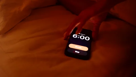Fingers Pressing Snooze Button on Smartphone Alarm Set for 6 AM on Bed in Dim Stock Footage 319250427