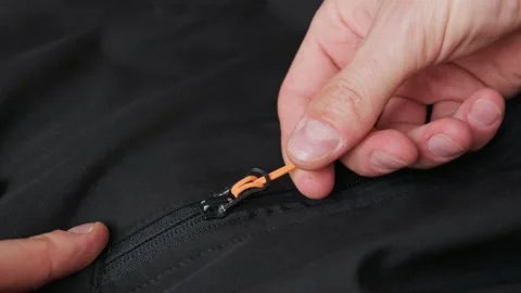 Fingers Pulling Orange Paracord Zipper Pull on Technical Black Garment 動画素材 338097740