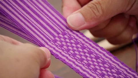 Fingers stringing and pressing purple and white yarn to create patterns on Stock Footage 218090951