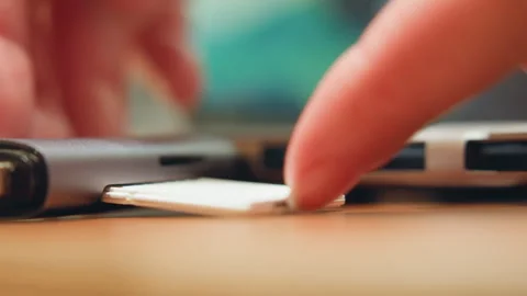 Fingertip carefully slides SD card into laptop for backup tasks. Warm desk Stock Footage 337365802