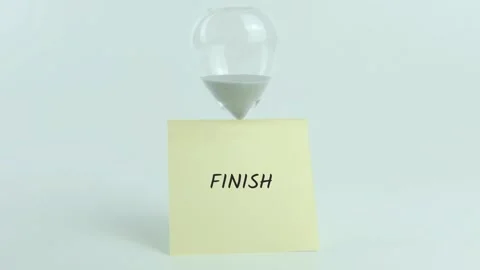 Finish written on yellow sticky note placed on hourglass on white background Stock Footage 313482950