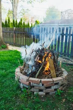 Fire in a backyard pit with smoke rising in the afternoon light surrounded .. Stock Photos