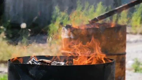 Fire burn in two iron barrels outdoors at sunny day. Man mixing in one of cask. Stock Footage 156726831